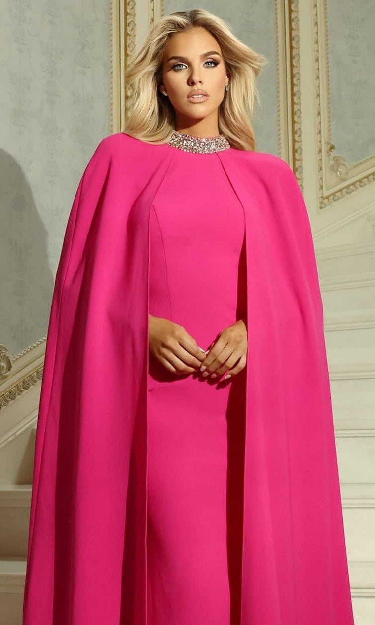 A woman stands indoors in front of an ornate, cream-colored wall and staircase, wearing the Jovani 46736 long prom dress—a bright pink crepe gown with a crystal-embellished collar.